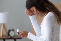 Unhappy stressed woman crying, feeling depressed, holding pregnancy test